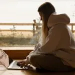 A person working remotely on a laptop by a lake, enjoying a tranquil outdoor environment.