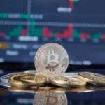 People gathered around a large screen displaying Bitcoin value charts and graphs in a modern tech hub.