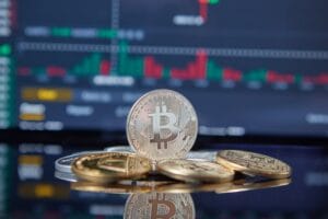 People gathered around a large screen displaying Bitcoin value charts and graphs in a modern tech hub.