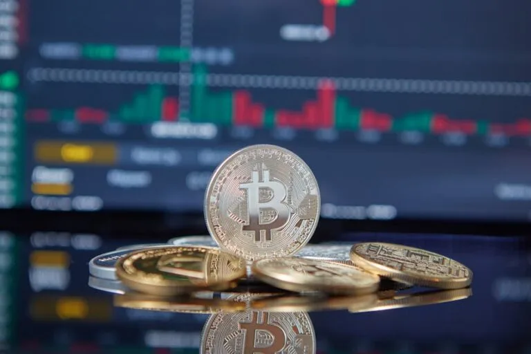 People gathered around a large screen displaying Bitcoin value charts and graphs in a modern tech hub.